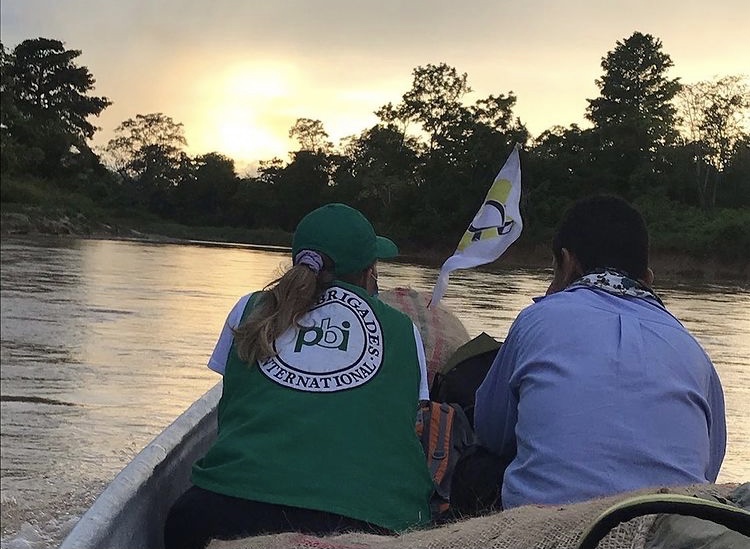 Elise sitter med ryggen til i en båt, med grønn PBI-vest på. Ved siden av sitter en mann i blå skjorte. Det er en vimpel med logoen ACVC-RAN på, og solnedgang i bakgrunnen.
